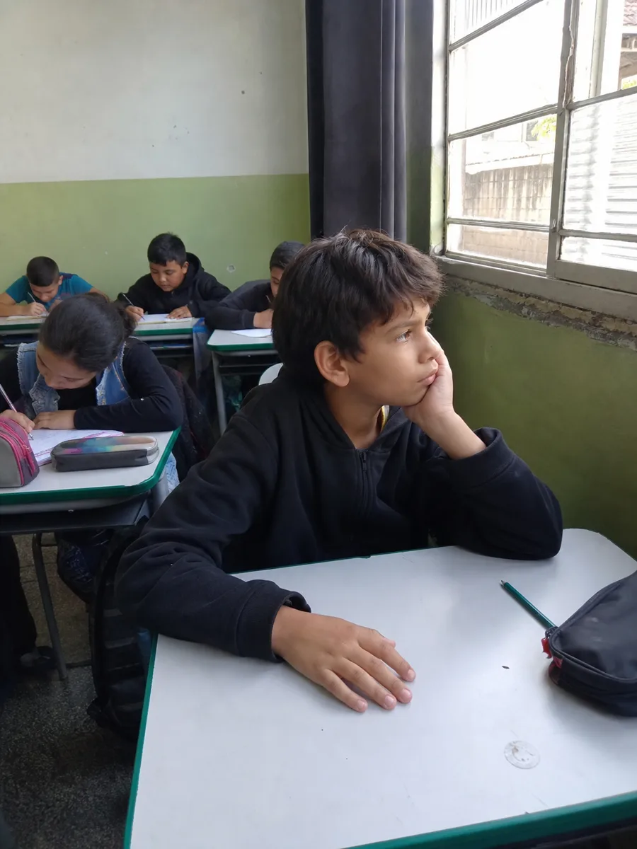 Menino na sala de aula olhando pela janela enquanto a turma escreve