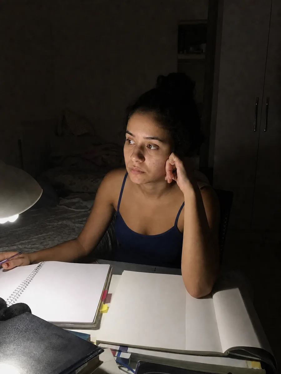 Jovem diante dos livros abertos, olhando pra longe, de madrugada